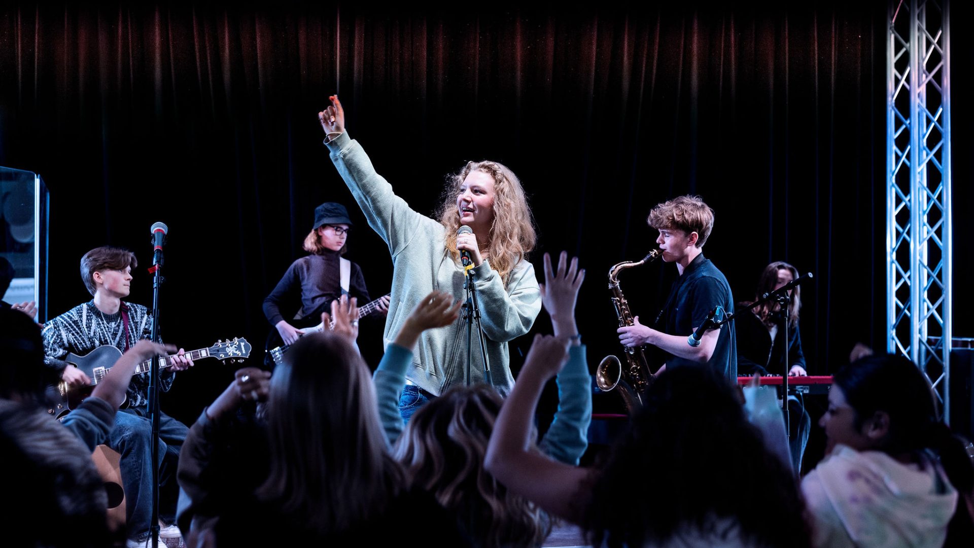 Ett band spelar på scenen och eleven som sjunger sträcker upp ena armen i luften.