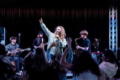 Ett band spelar på scenen och eleven som sjunger sträcker upp ena armen i luften.
