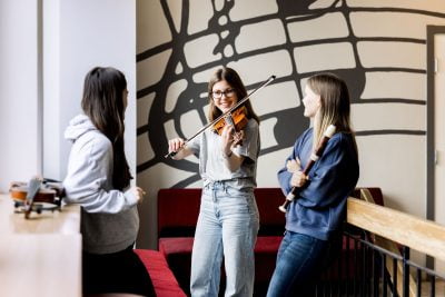 Tre elever på Pops Academy övar på sina instrument i korridoren.