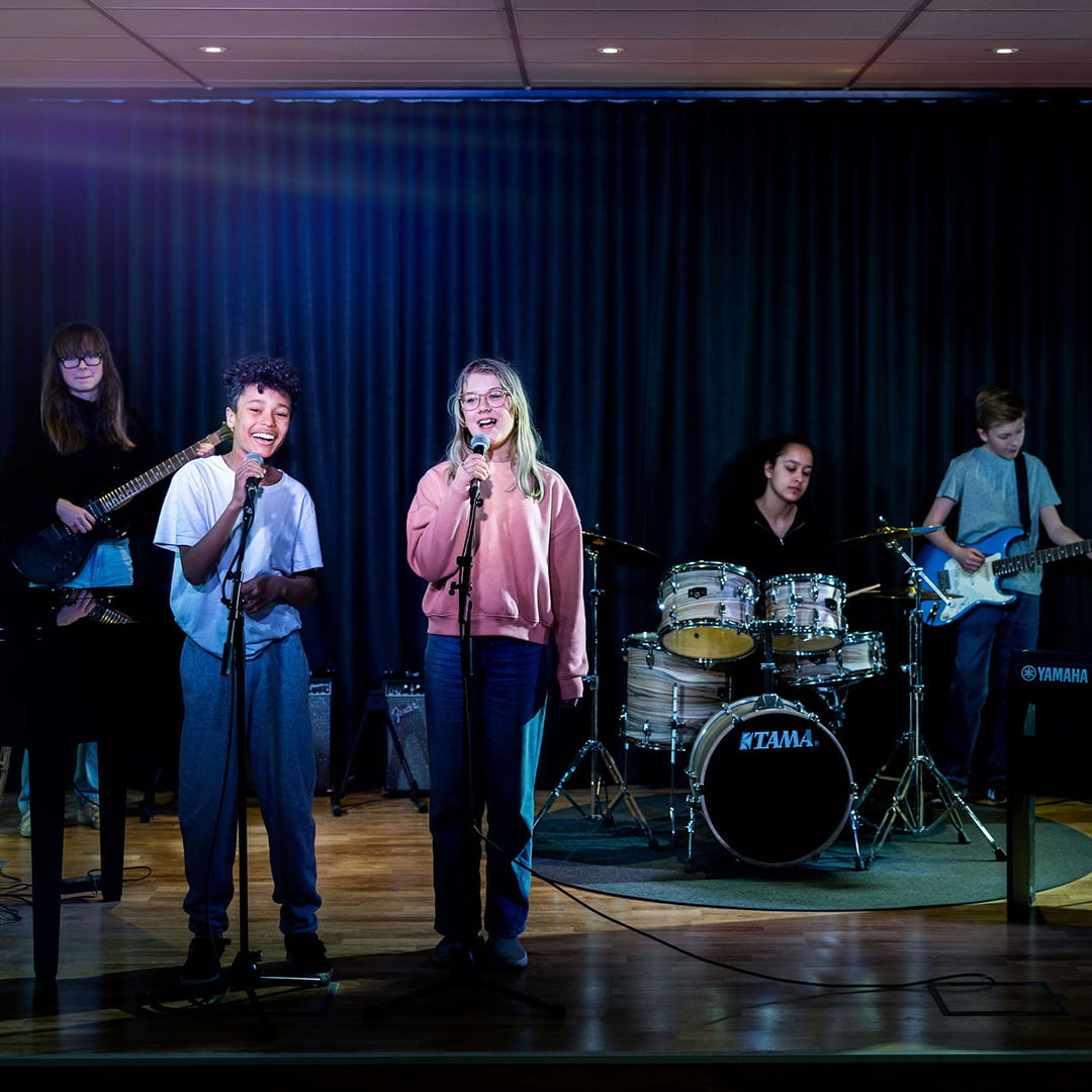 Ett band av elever på Pops Academy sjunger och spelar tillsammans på scen.