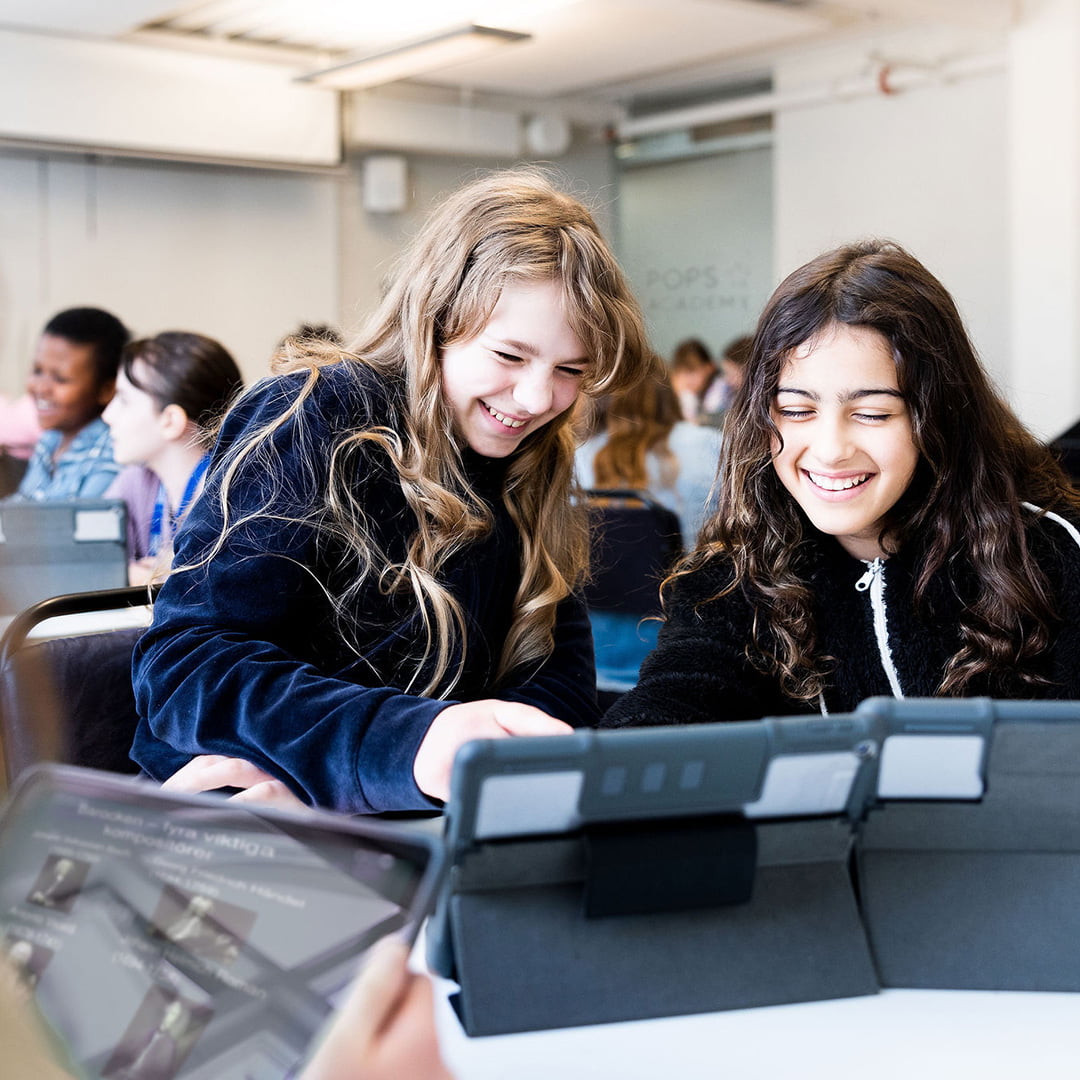 Två elever på Pops Academy studerar tillsammans vid läsplattor.