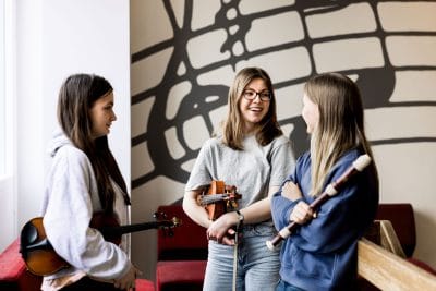 Tre elever står i korridoren med sina instrument.