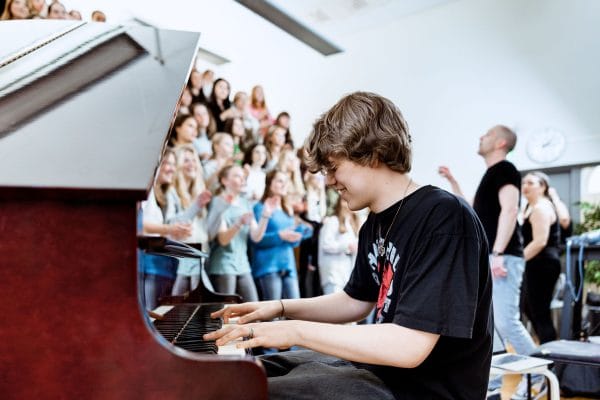 Elev spelar piano med en kör som sjunger bakom sig.