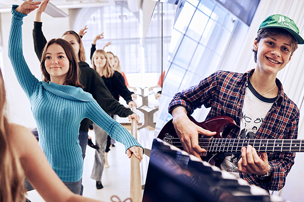 I vänstra delen av bilden är det flera elever som dansar. I högra delen av bilden spelar en elev elgitarr.