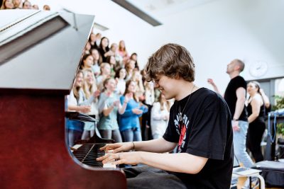 Elev på Pops Academy spelar piano och en kör sjunger i bakgrunden.