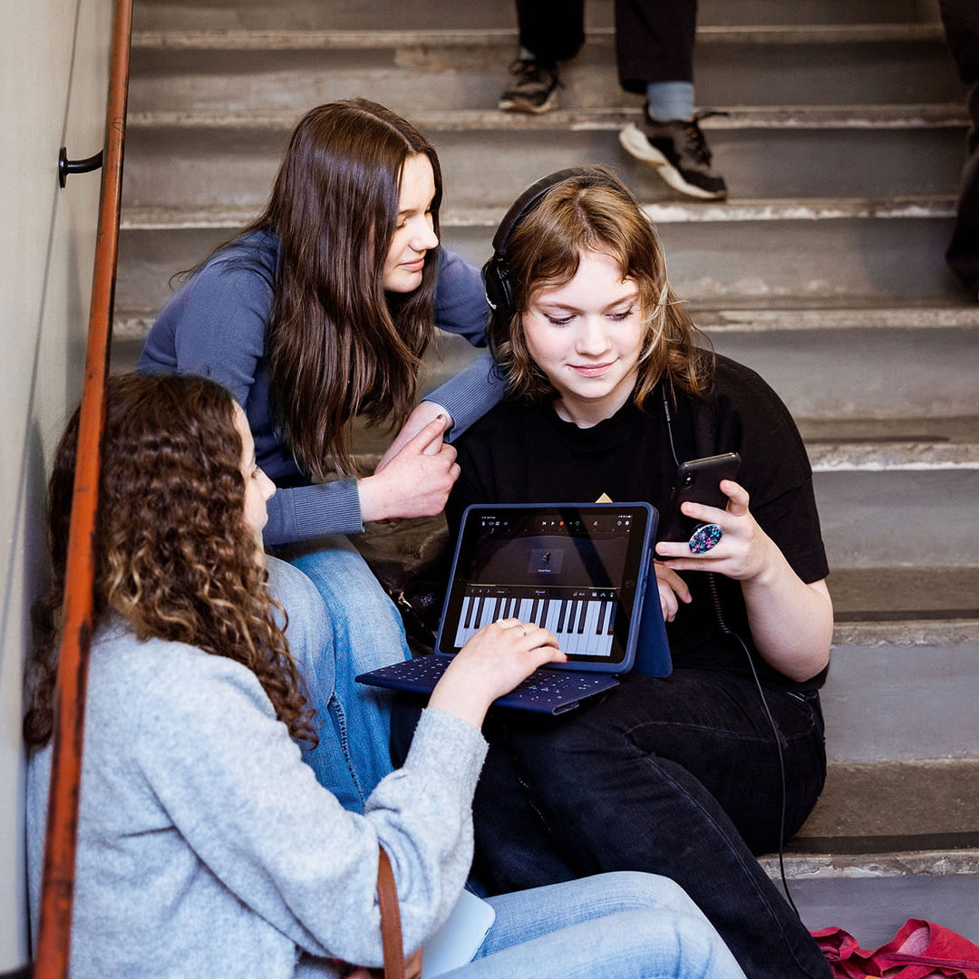 Tre elever på Pops Academy sitter och skapar musik i trapphuset.