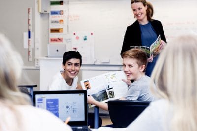 Elever sitter i klassrummet med laptops och läroböcker.