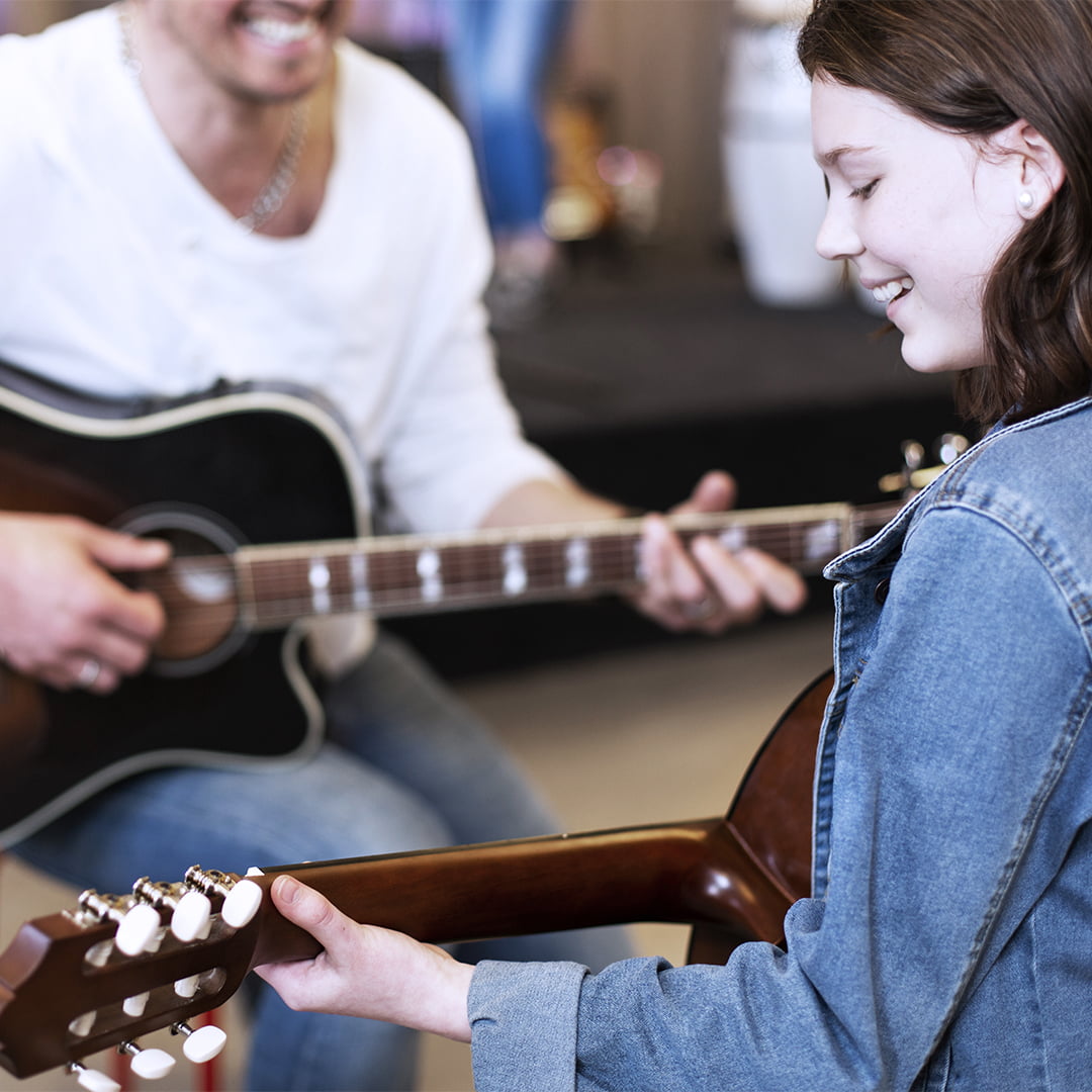 Elev övar på att spela gitarr tillsammans med musiklärare